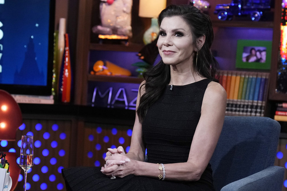 Heather Dubrow, wearing a black dress, sits on Watch What Happens Live with her hands folded in her lap 